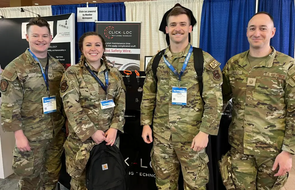 Click-Loc challenge at Logistics Officer Association (LOA) Symposium event in 2024. Four military personnel in camouflage uniforms standing in front of a trade show booth with banners displaying "Click-Loc" safety wire products.